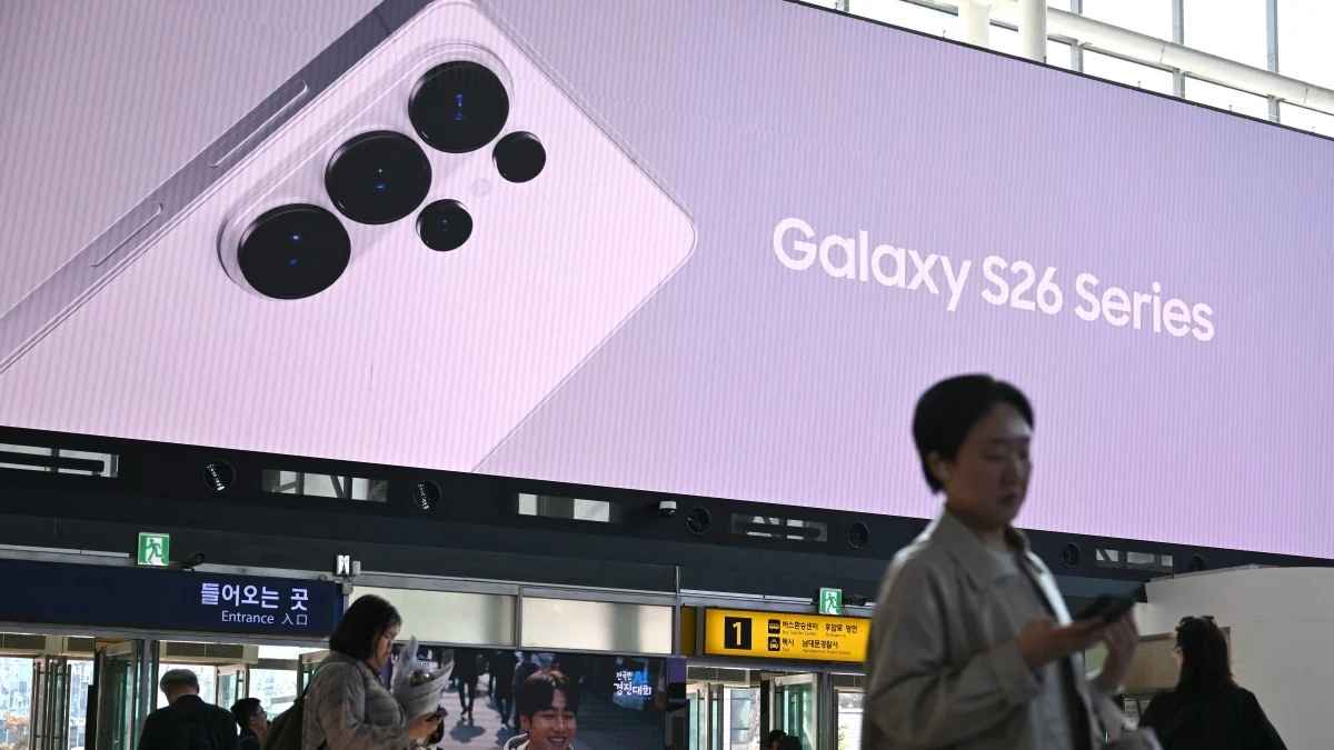A large digital billboard in a subway station displays a Samsung Galaxy S26 Series phone with a purple back and circular camera array, with pedestrians walking below.