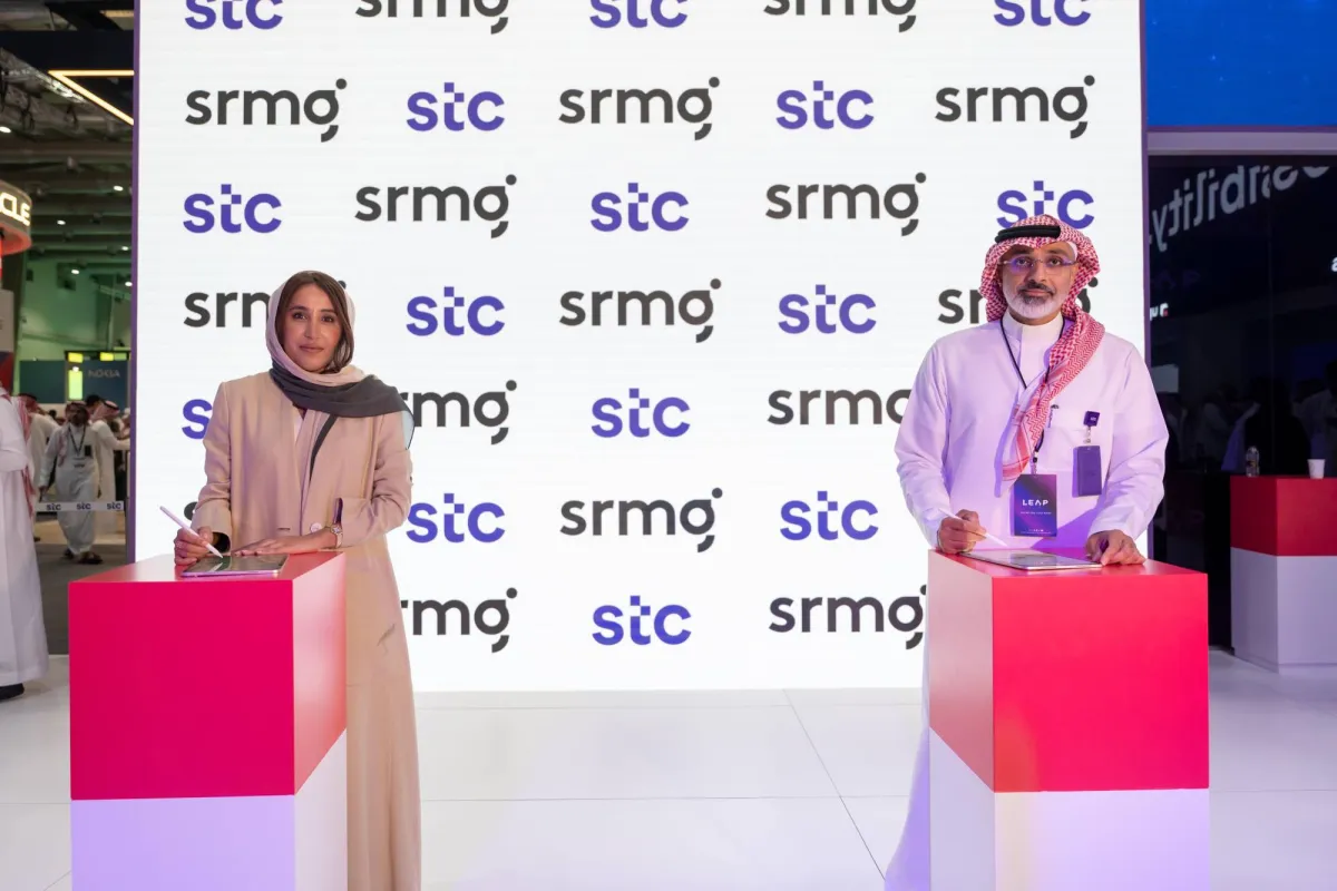 Two people stand at podiums with pink fronts in front of a branded backdrop displaying "stc" and "srmo" logos at what appears to be a conference or press event.