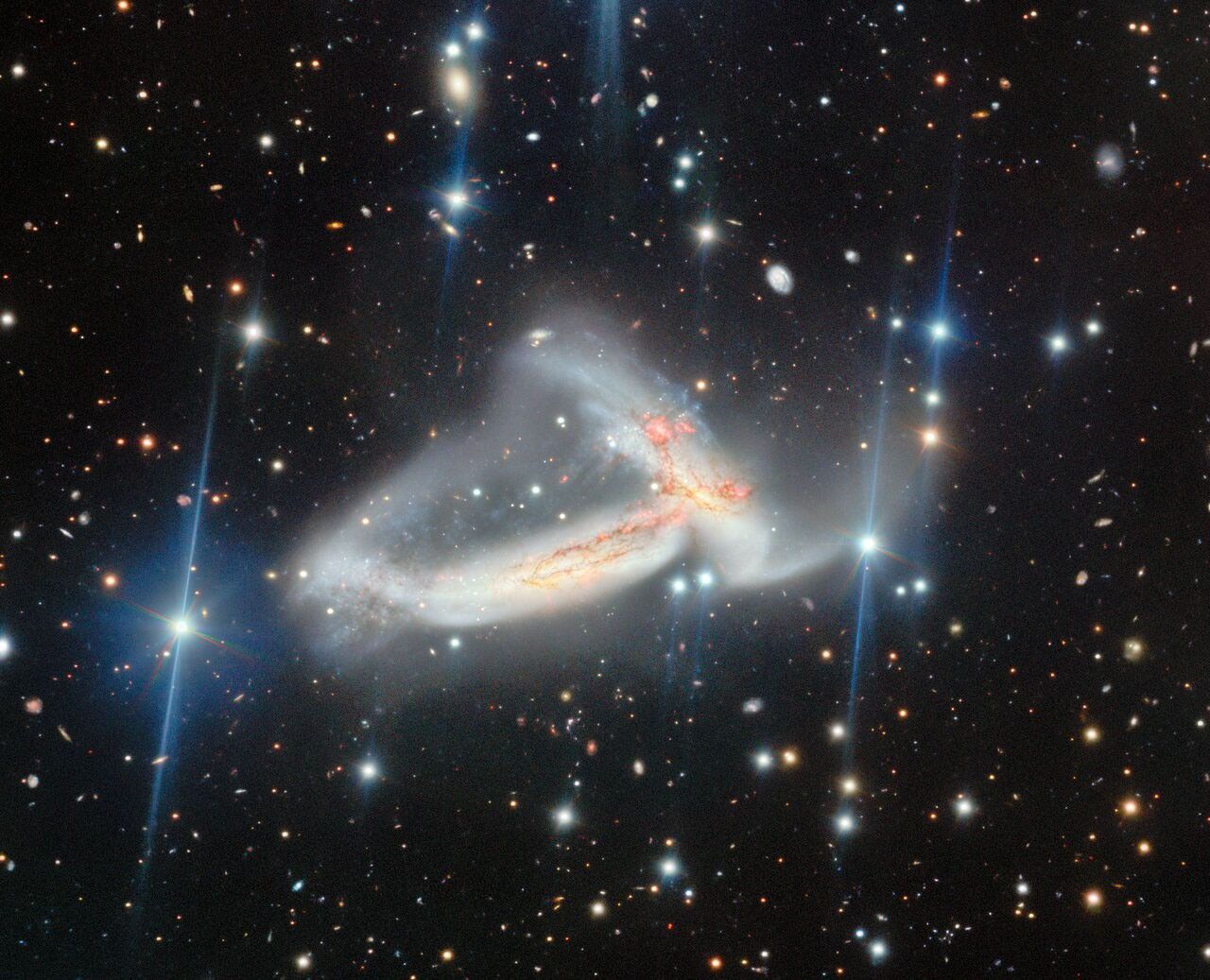 Two galaxies colliding in space, surrounded by stars, with white and gray streaks from one galaxy merging into orange and red tones from the other.