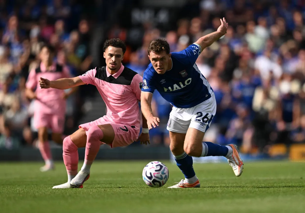 A player in a blue jersey with the number 26 controls the ball while being challenged by an opponent in a pink jersey during a soccer match.